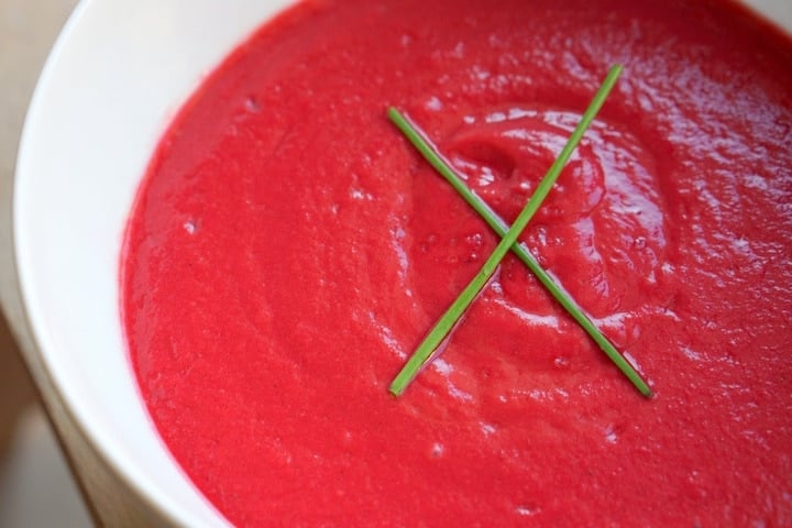 A white bowl filled with bright purple cold beet soup with chives on top.