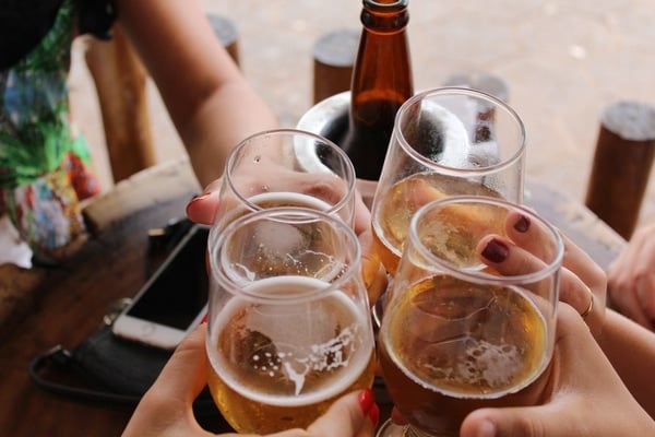 Close-up of four beer glasses raised together in a toast above an outdoor wooden table.