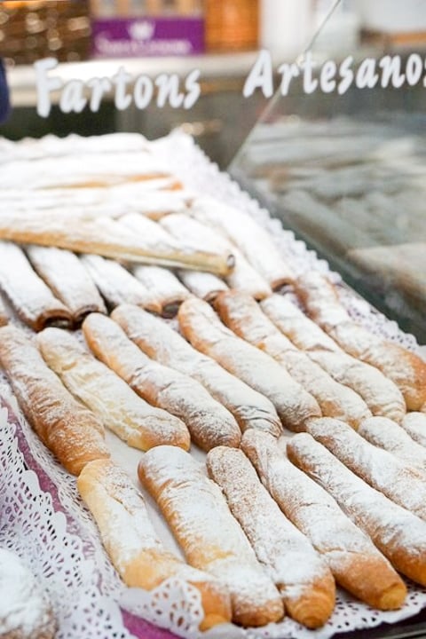 A display of elongated pastries dusted with powdered sugar, with a sign reading "Fartons Artesanos."