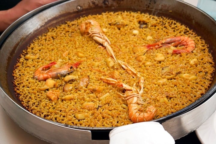 Close-up of a large round pan of seafood paella with yellow rice and giant prawns.