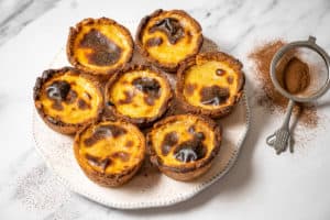 Pasteis de nata o na white plate with a sifter of cinnamon on the side.