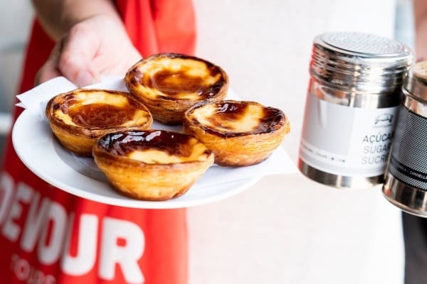 Close-up of four pastéis de nata on a plate held by a Devour Tours guide.