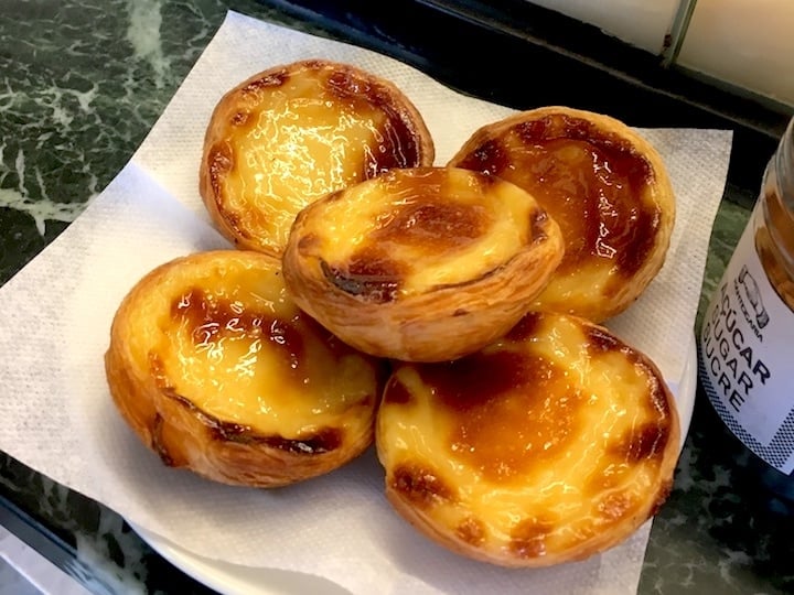 Close-up of five custard tarts with caramelized tops, sitting on a napkin.