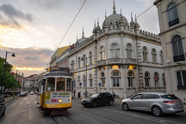 A yellow tram passing by an ornate building at sunset in Príncipe Real, Lisbon.