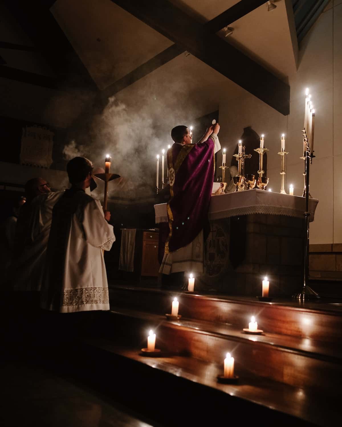 A priest celebrating mass in a church lit with many candles