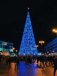 Large blue Christmas tree lit up at night in a busy city square