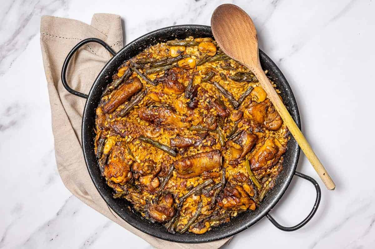 Overhead shot of paella with chicken and veggies in a round pan with a wooden spoon.