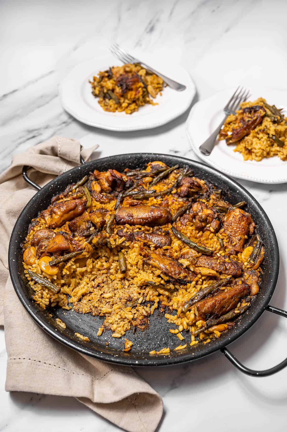 Spanish rice with vegetables and chicken in a big paella pan with two servings on plates.