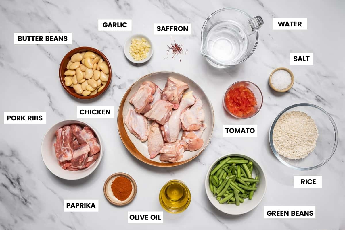 Ingredients to make Valencian paella on a white marble countertop.