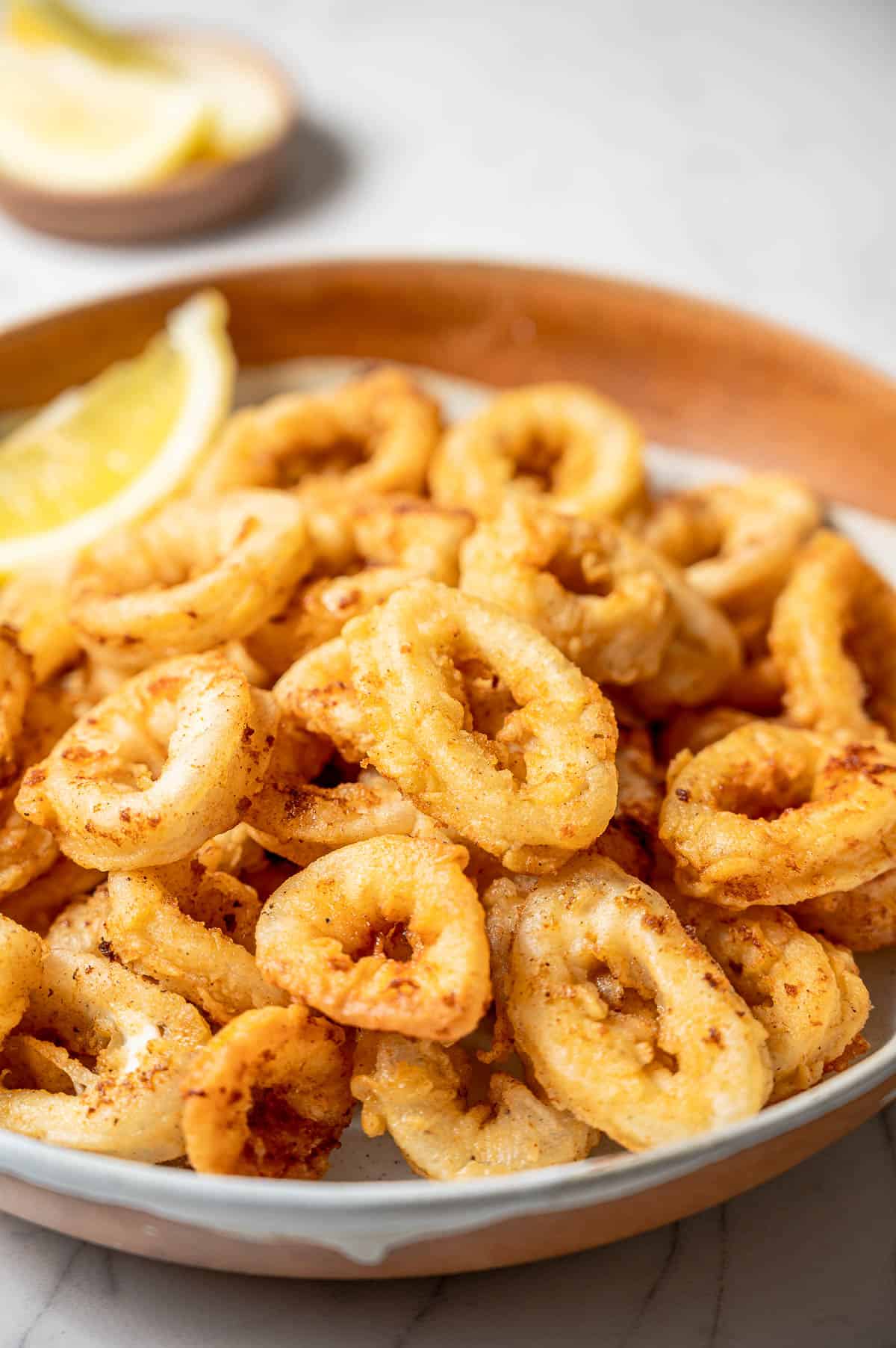 A bowl of fried calamari rings with lemon wedges.