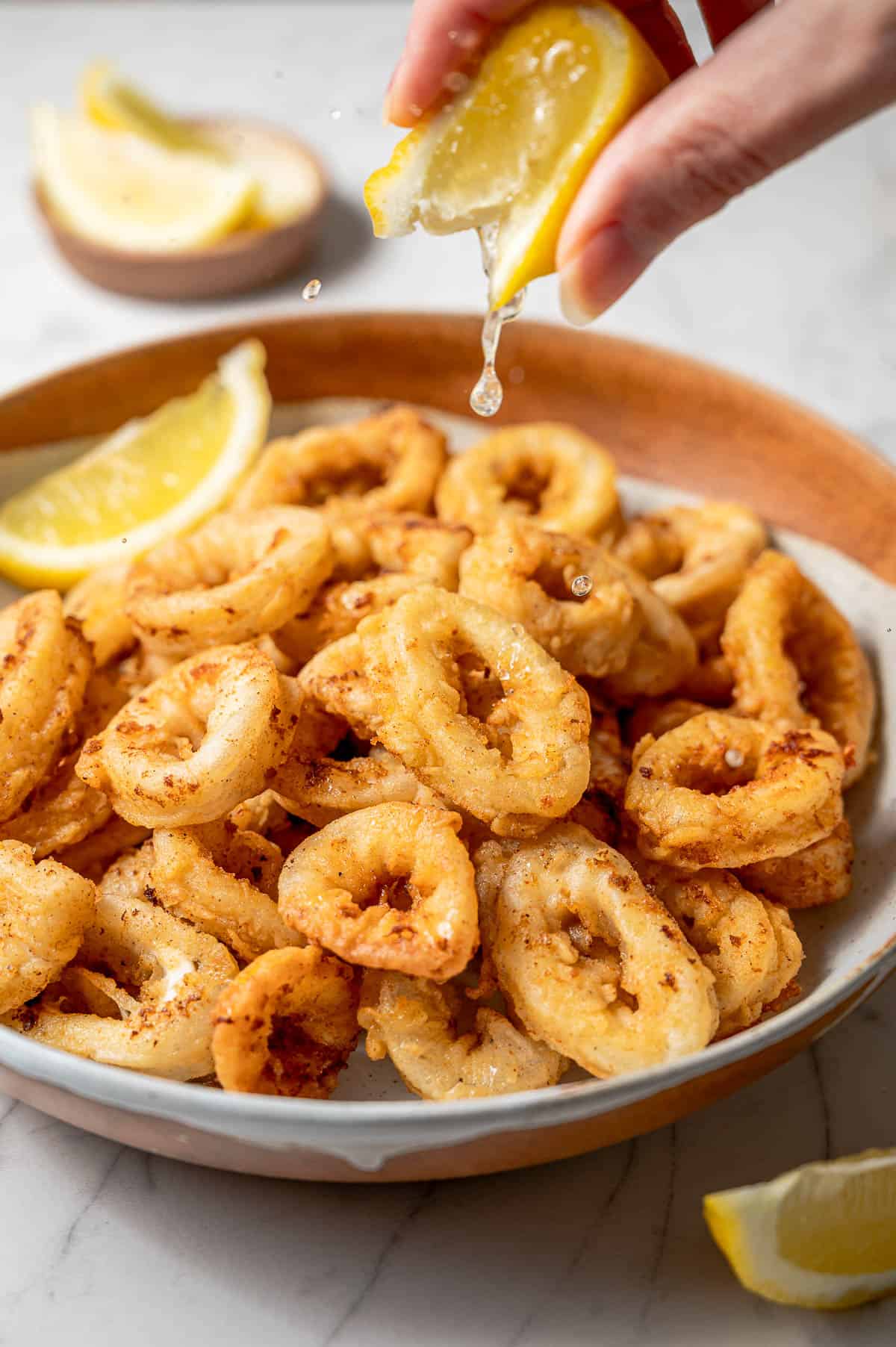 A large bowl of fried calamari with a hand squeezing lemon on top.