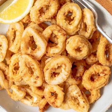 A big plate of fried calamari with a lemon wedge.