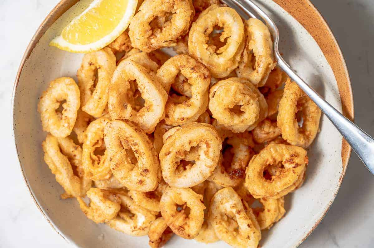 A big plate of fried calamari with a lemon wedge.