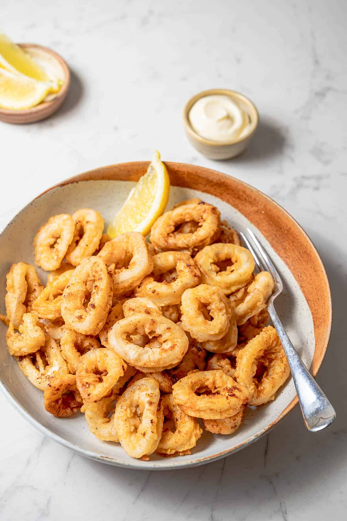 A large bowl of fried calamari rings with a lemon wedge and a fork.