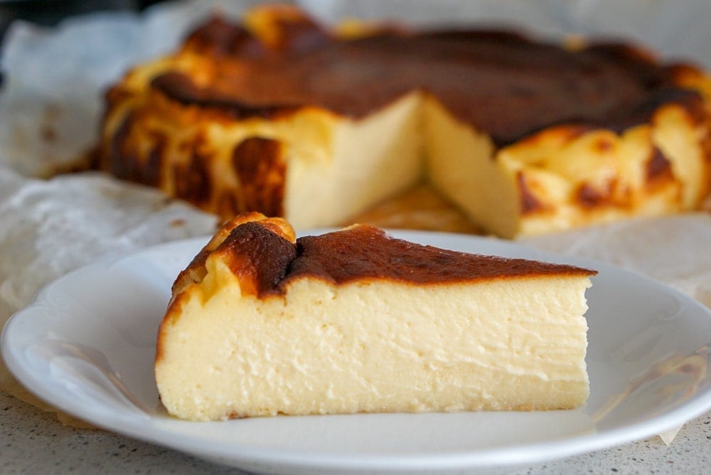 A slice of creamy crustless cheesecake with a burnt top, with the whole cheesecake behind it.