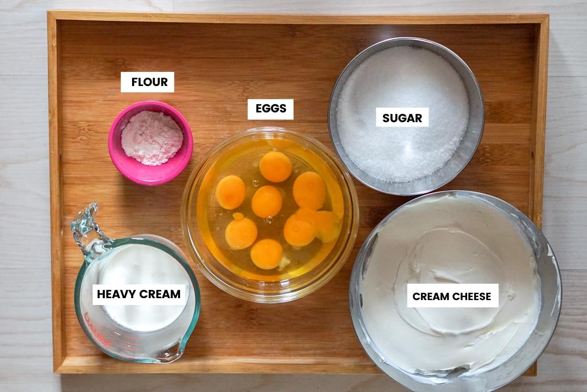 Burnt Basque cheesecake ingredients on a wooden tray: flour, eggs, sugar, cream cheese and heavy cream