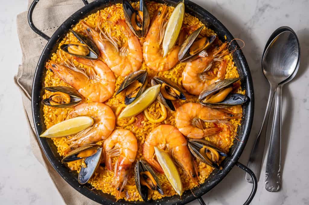 Overhead shot of seafood paella in a black paella pan with calamari, mussels, shrimp and lemons.