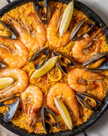 Overhead shot of seafood paella in a black paella pan with calamari, mussels, shrimp and lemons.