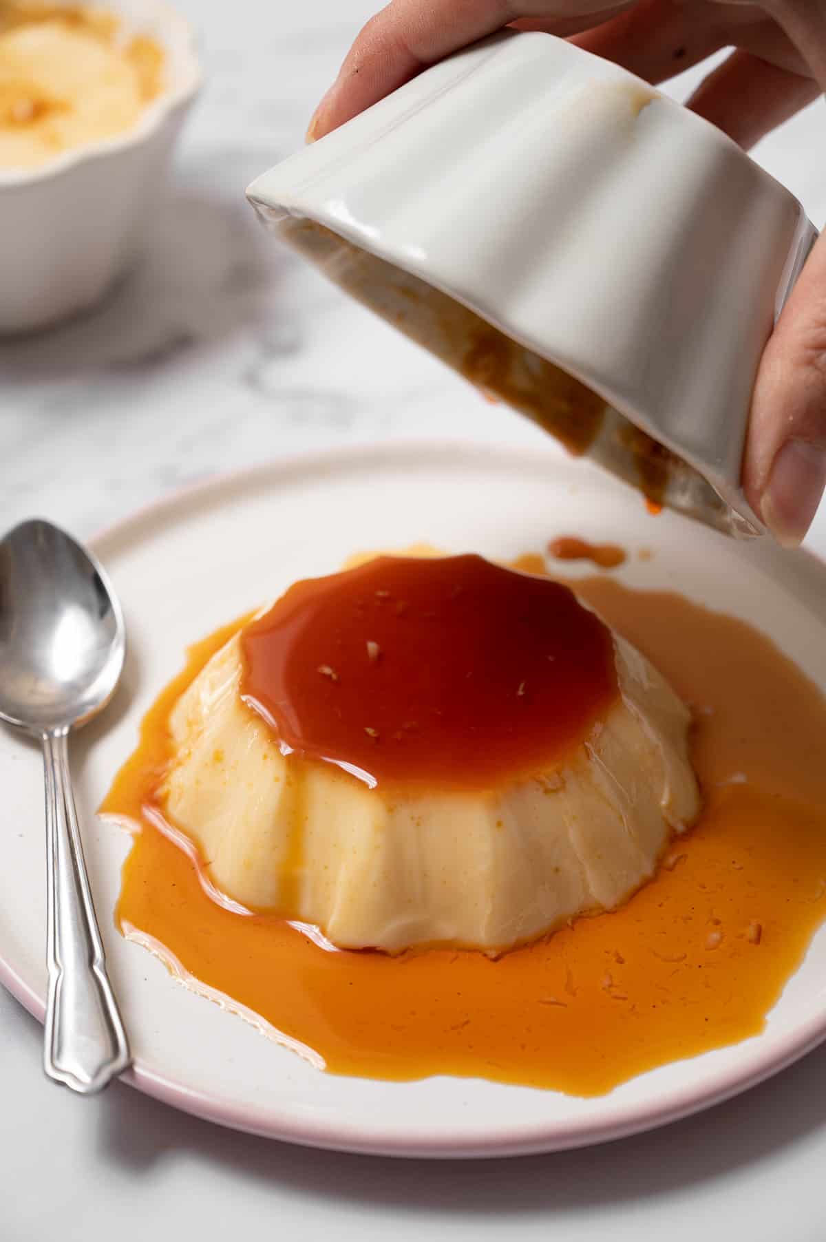 Spanish flan coming out of the mold onto a white plate.