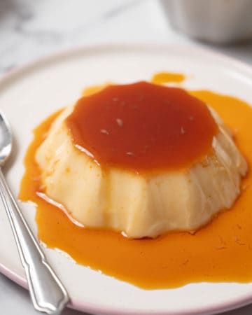 Traditional Spanish flan on a white plate covered in caramel syrup.