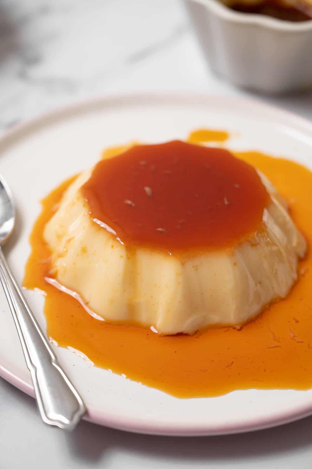 Traditional Spanish flan on a white plate covered in caramel syrup.