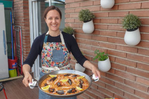 Woman holding a large pan of seafood and chorizo paella.