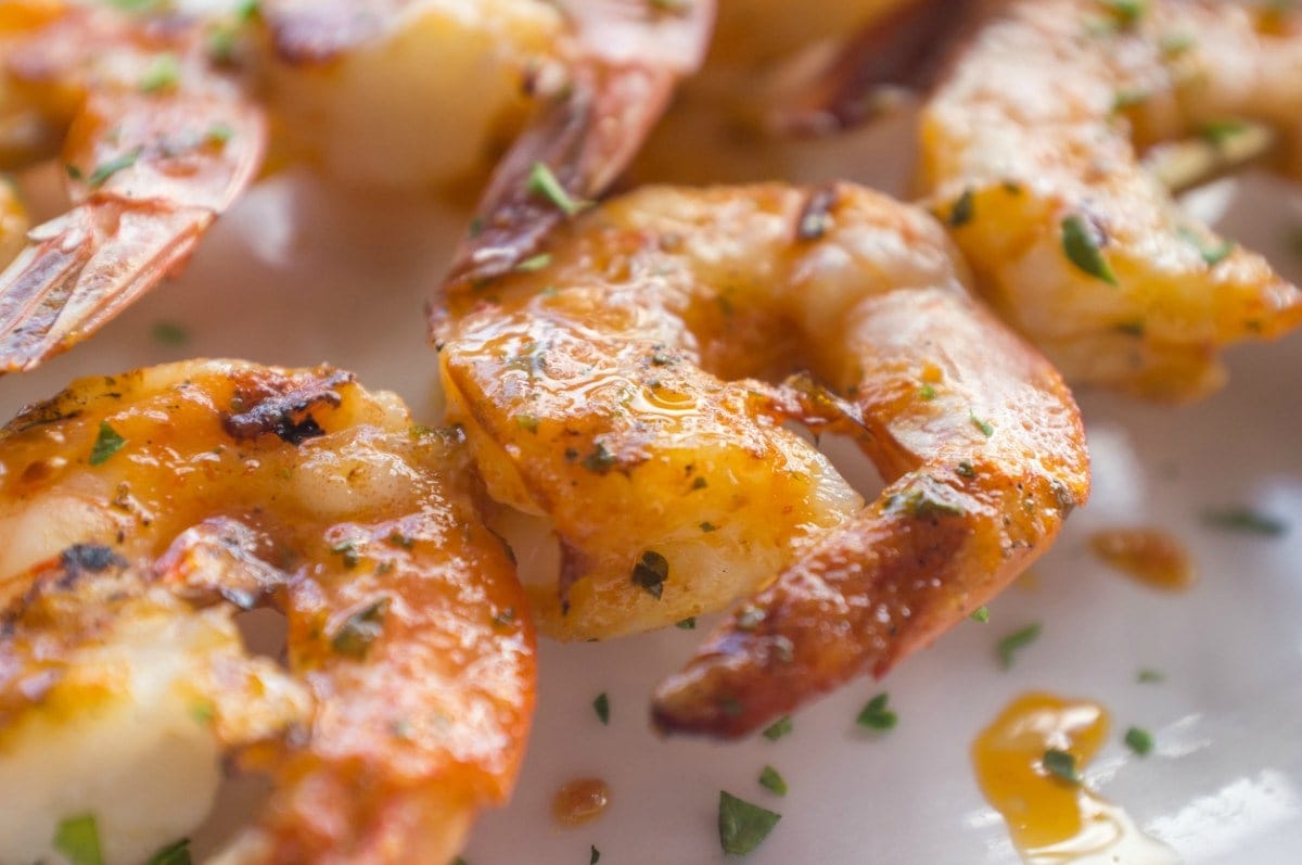 Close-up of skewered cooked shrimp covered in olive oil, garlic, and herbs.