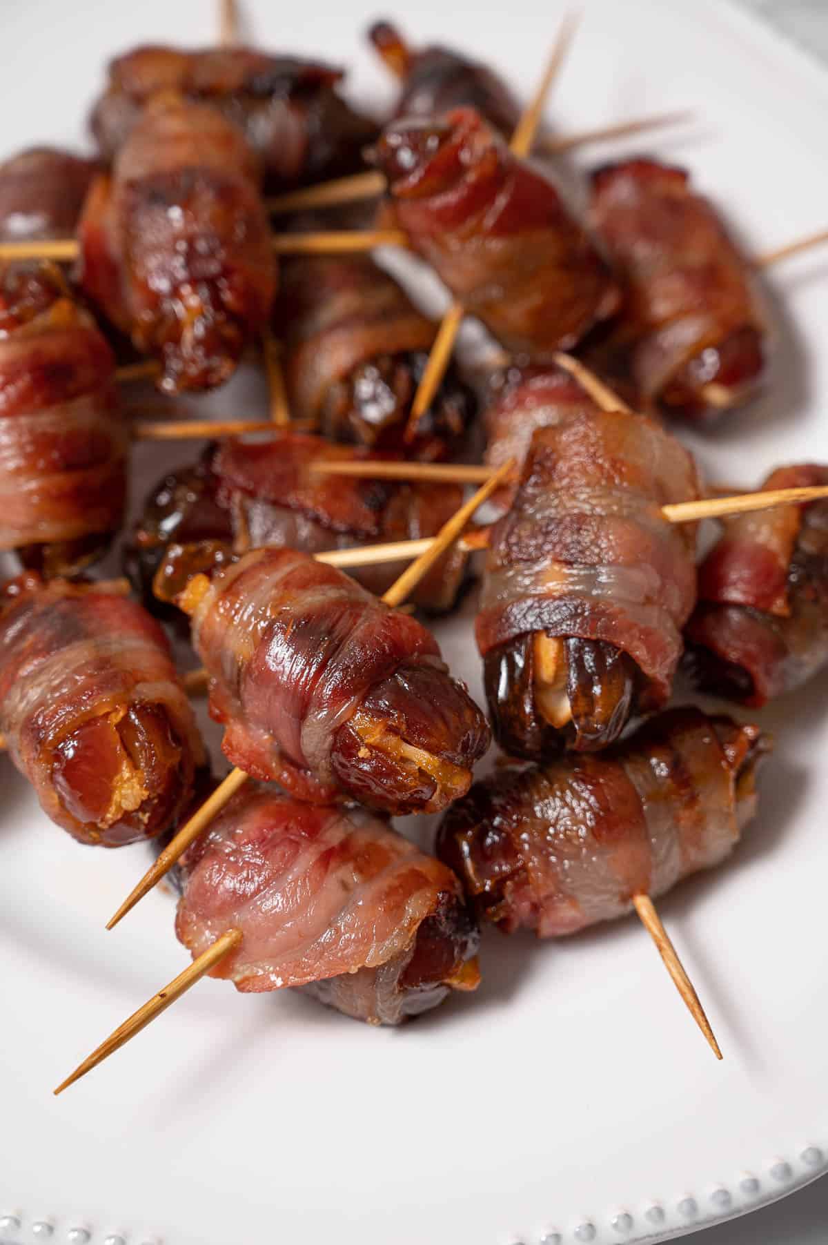Bacon wrapped dates on a white plate.