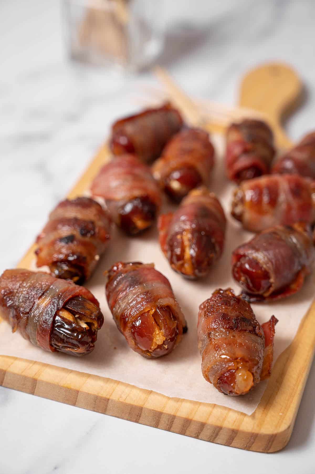 Several bacon-wrapped dates on a wooden platter.