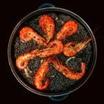 Overhead shot of black paella with bright red prawns