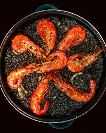 Overhead shot of black paella with bright red prawns