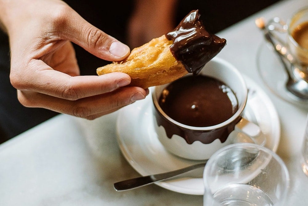 Close-up of someone holding a thick piece of fried dough after dipping it in hot chocolate.