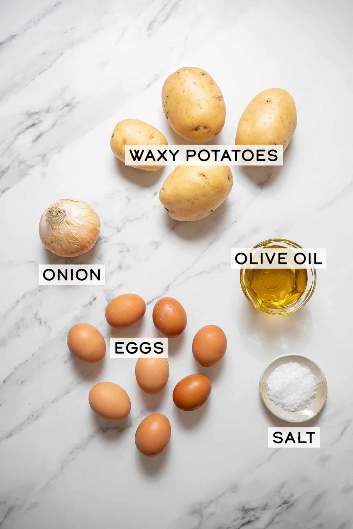 onion, potatoes, eggs, and bowls of oil and salt on a white marble surface.
