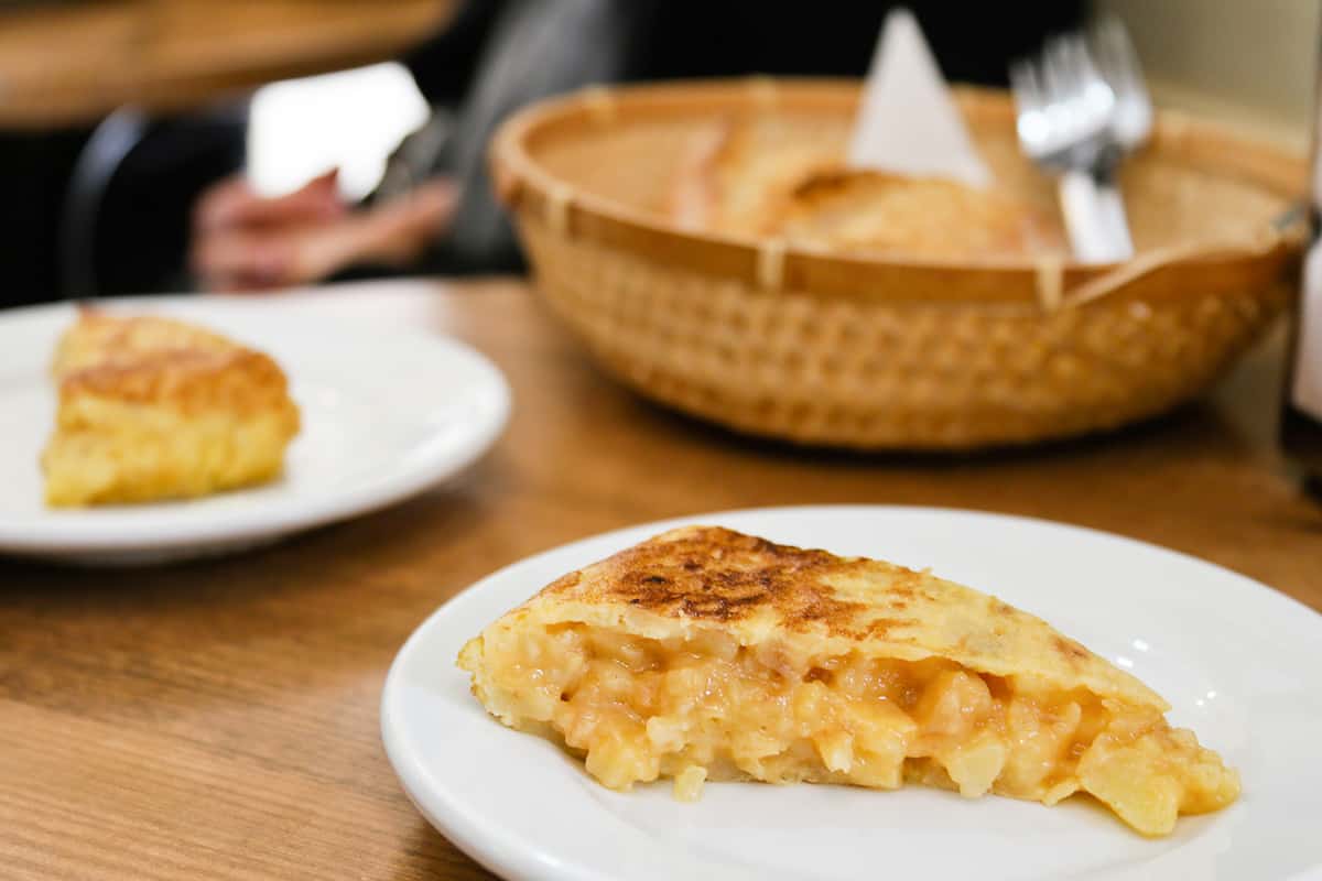 Two slices of potato omelet on white plates, with gooey centers and golden brown tops.