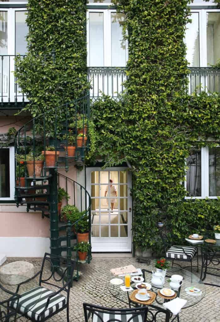 As Janelas Verdes hotel courtyard with cafe tables, an iron spiral staircase, and lots of plants