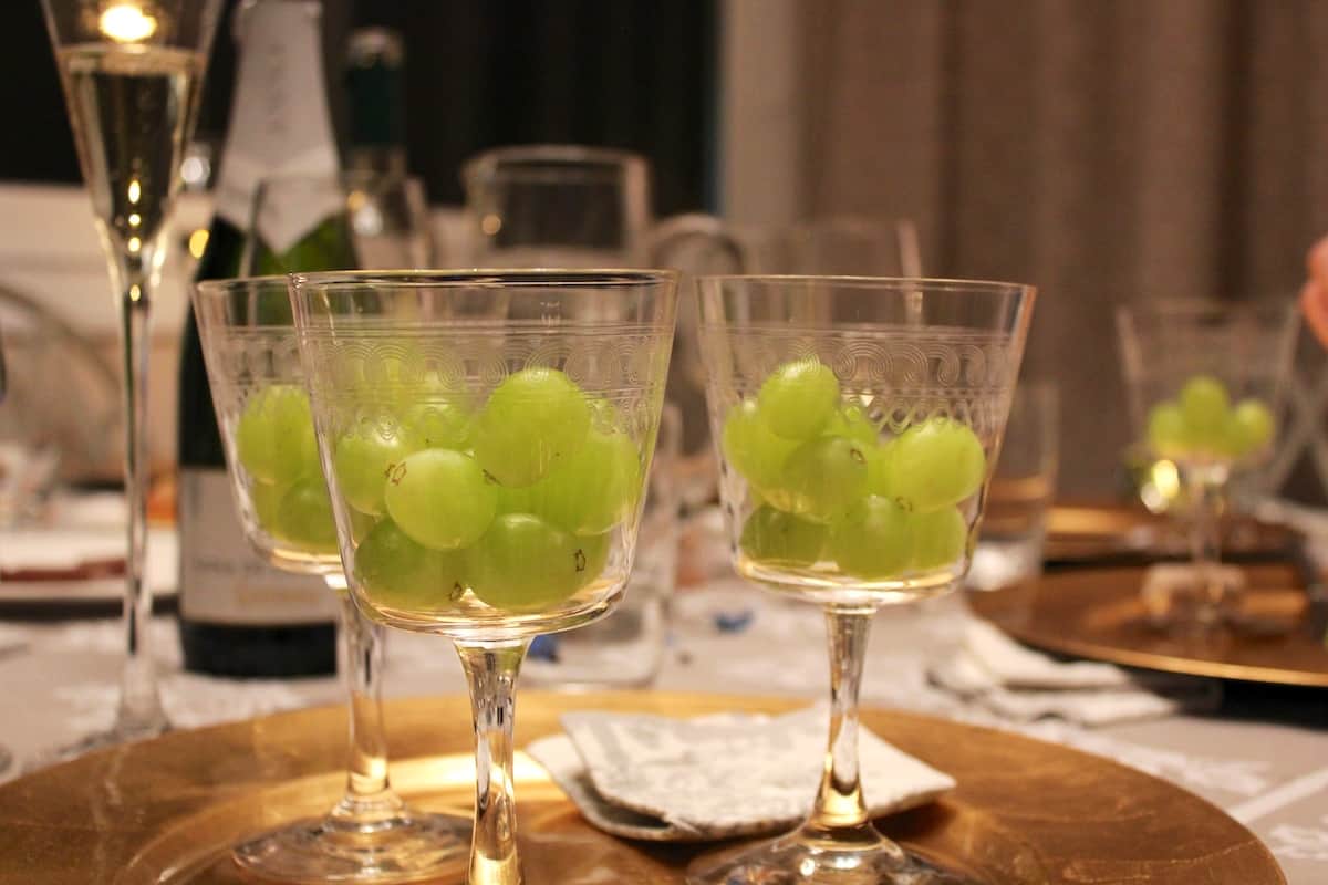 Several clear glasses on a dining table, each filled with 12 green grapes.