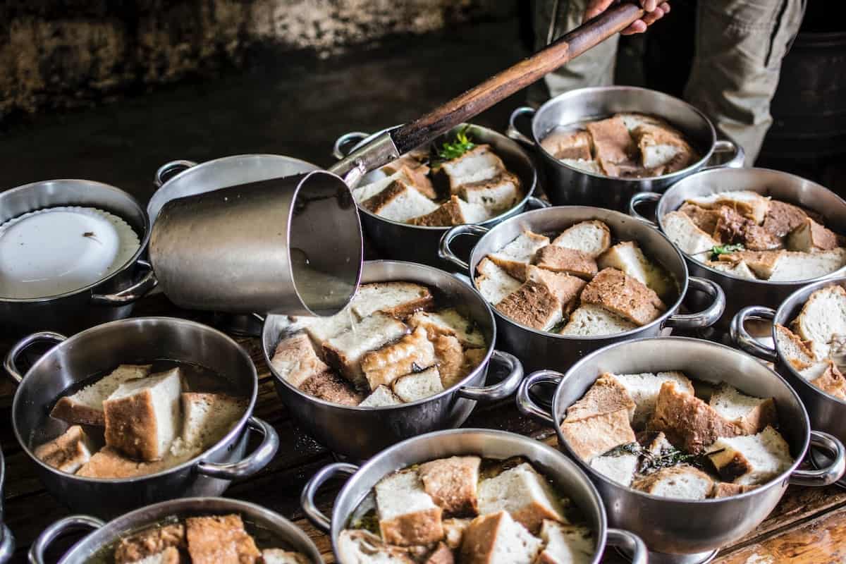 Pots of garlic soup with bread chunks simmering on a stove.