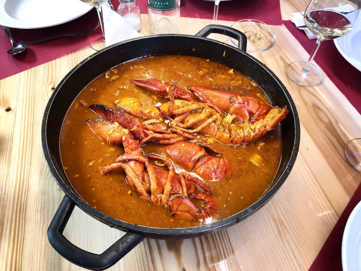 Large pot of soupy rice with lobster on a wooden tabletop.