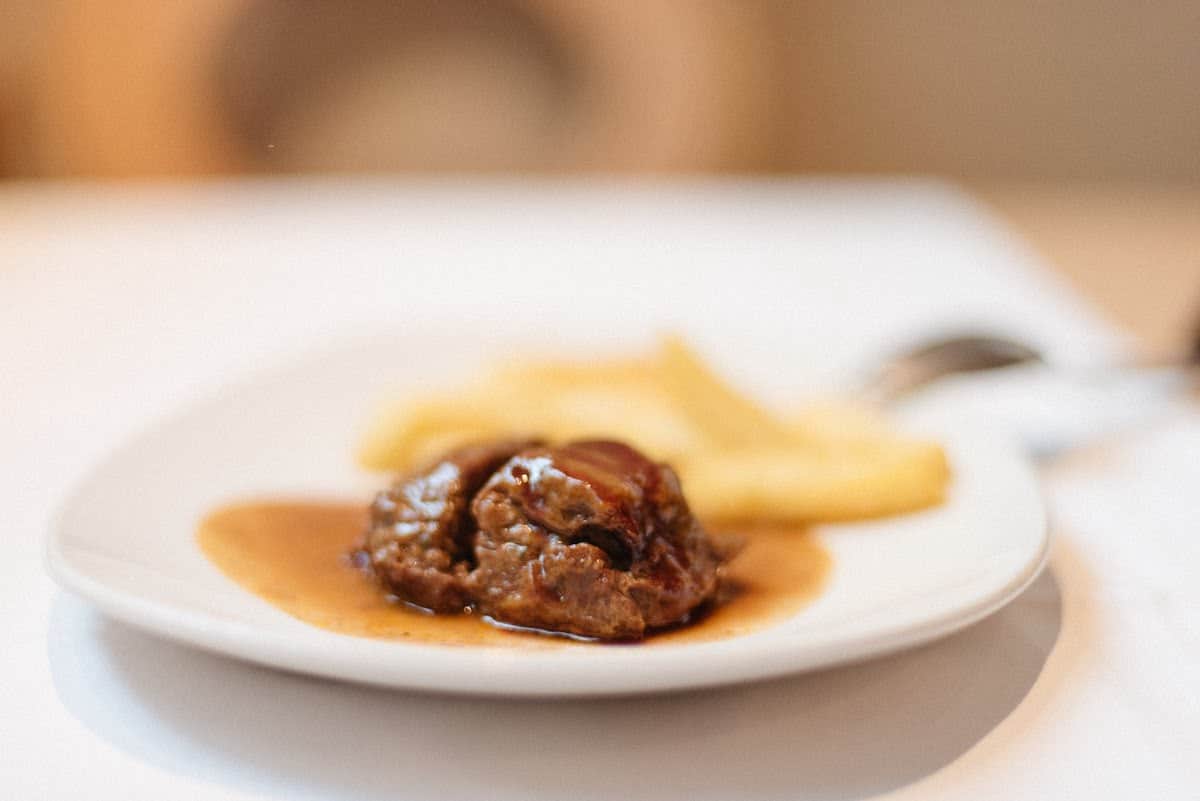 Braised pork cheek in sauce next to french fries on a white plate.