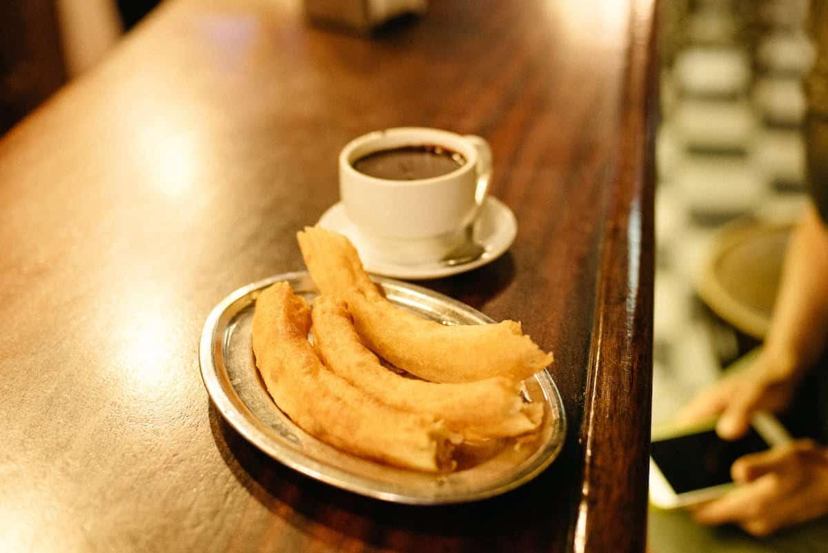 Plate of churros next to a mug of hot chocolate on a wooden bar top.