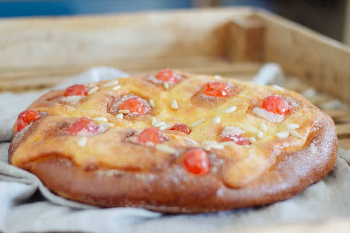 Close-up of a round sweet flatbread garnished with red candied cherries and pine nuts.