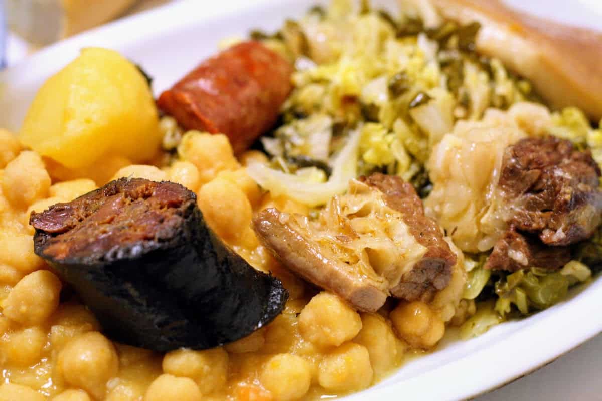 Stew of sausages, chickpeas, and vegetables on a white plate.