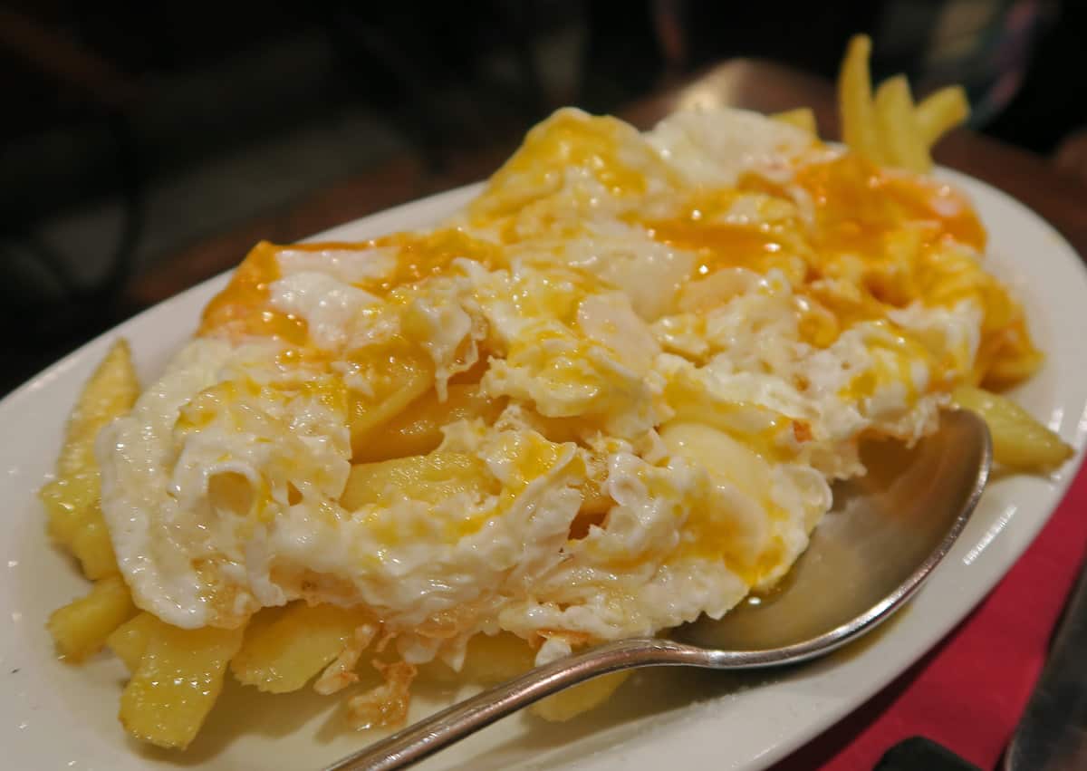 Fried potatoes topped with runny fried eggs and served on a white plate.