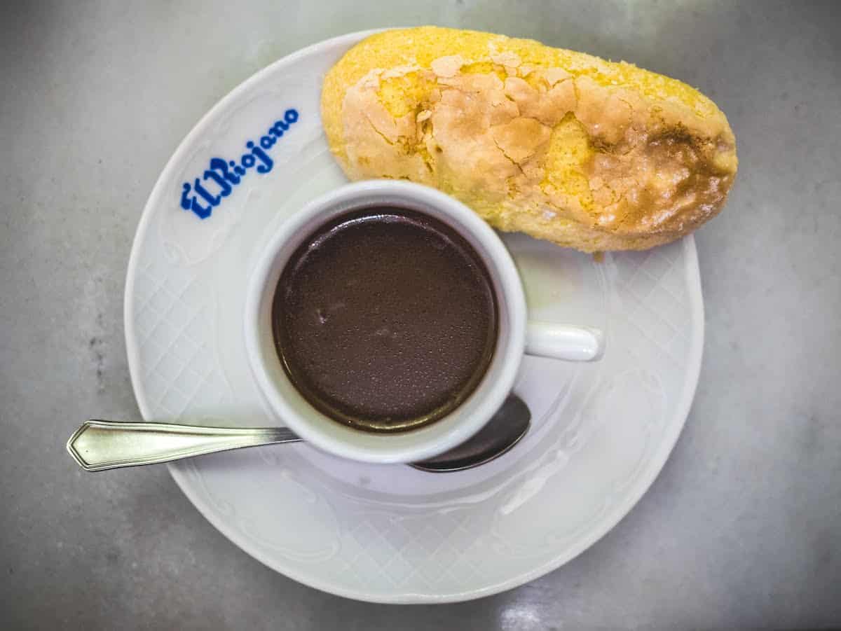 Overhead shot of a mug of thick hot chocolate beside a ladyfinger cookie on a white plate.