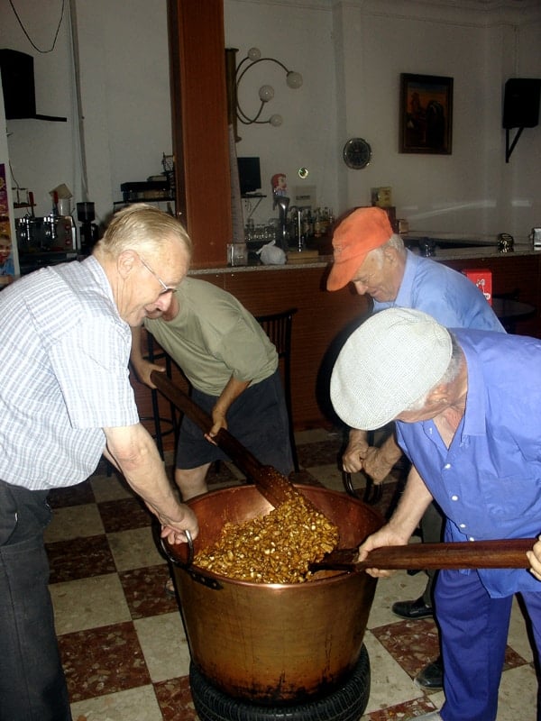 Four older men stir a huge vat of piñonate with wooden spoons