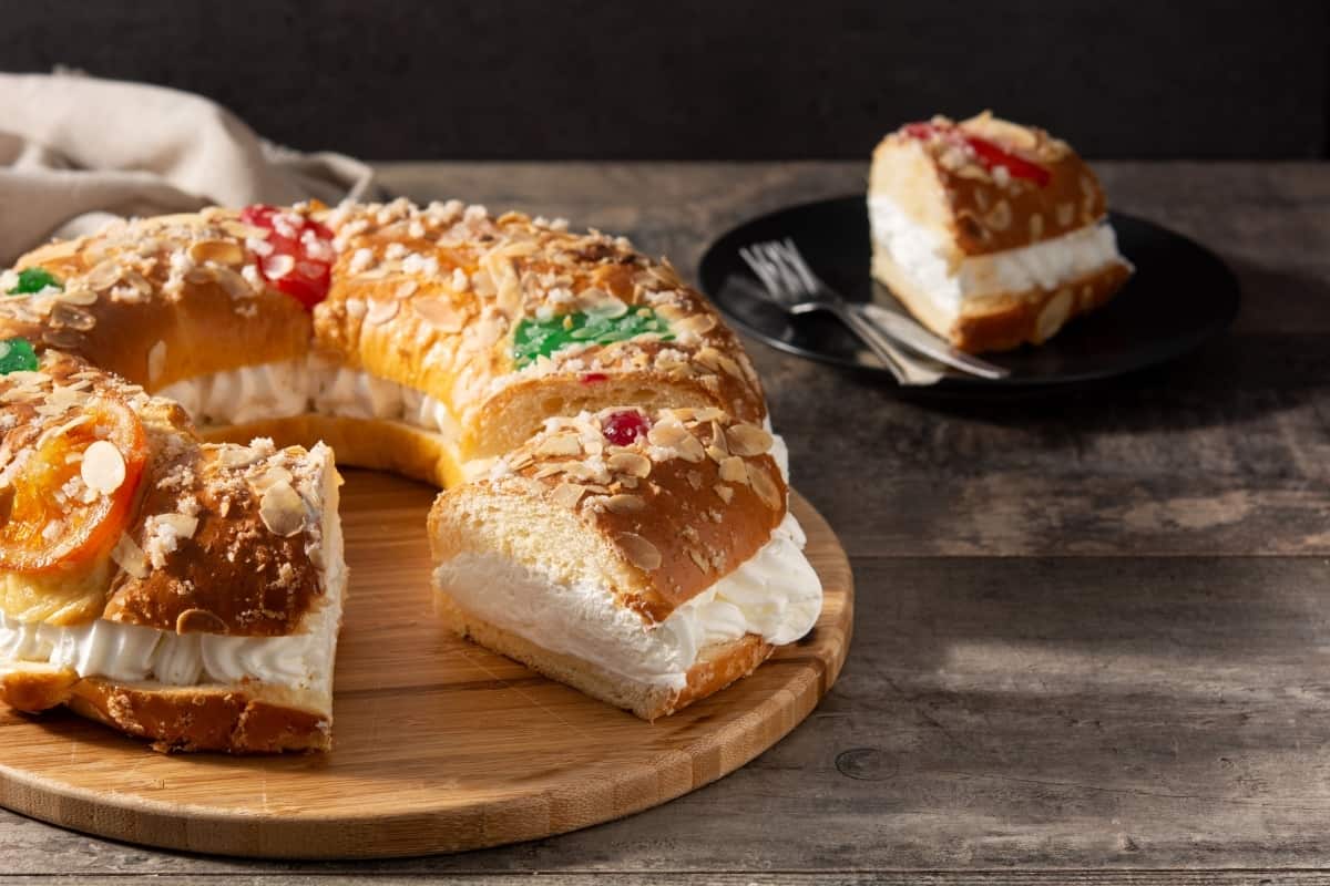 Roscon de Reyes stuffed with whipped cream on a counter with a plate with a slice behind it. 