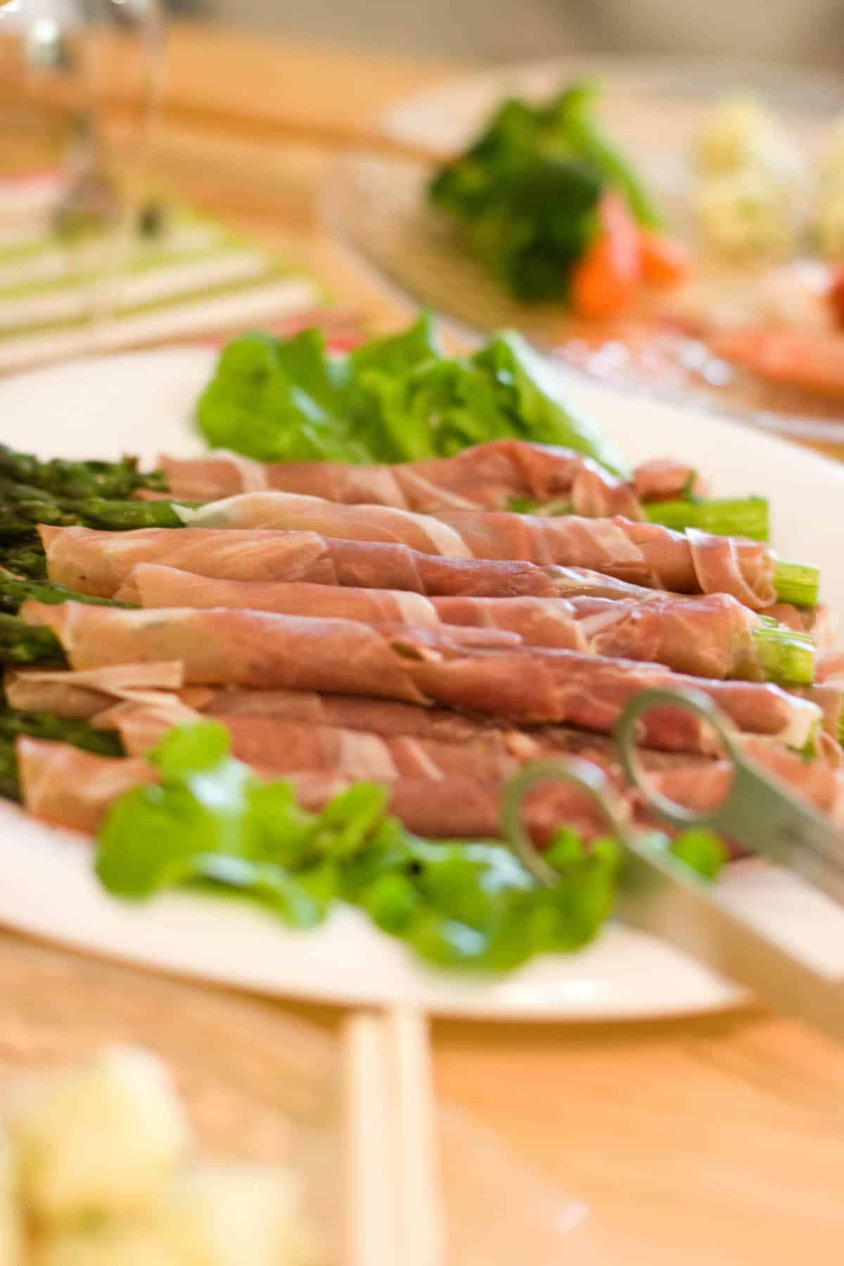 Green asparagus spears wrapped in slices of cured ham on a white plate.