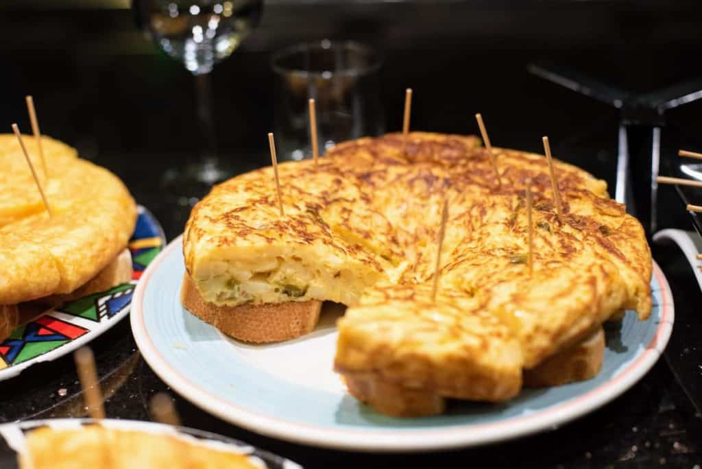 Slices of potato and green pepper omelet served skewered atop pieces of bread.