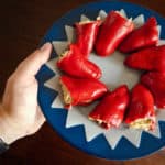 A person's hand holding a blue and white plate of red peppers stuffed with tuna