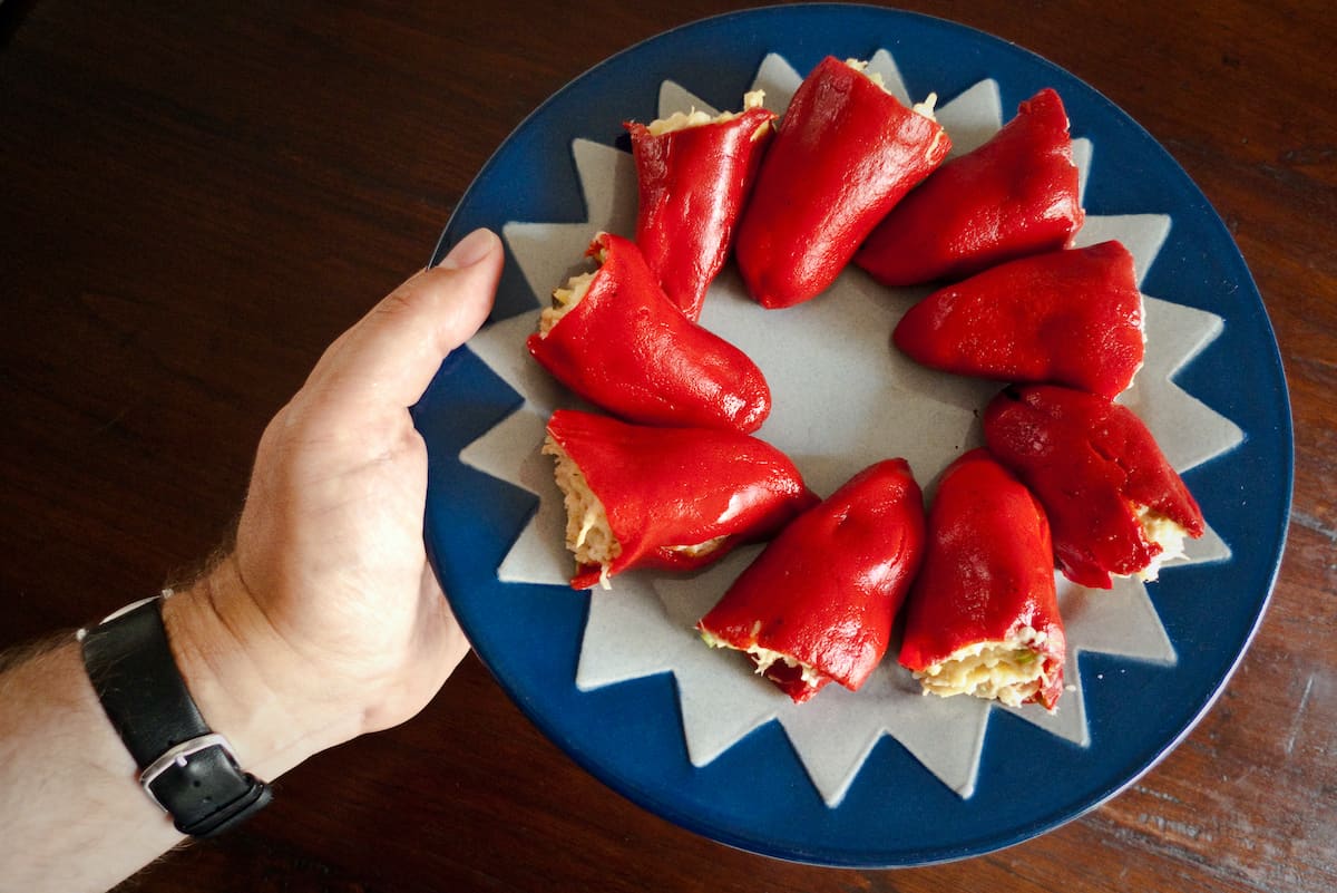 A person's hand holding a blue and white plate of red peppers stuffed with tuna